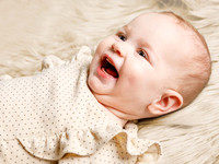 Baby girl lays on a cream blanket and smiles off-camera