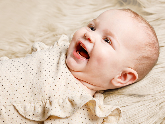 Baby girl lays on a cream blanket and smiles off-camera