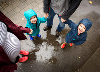 Family hold hands and look up past mum's baby bump while rain falls around them