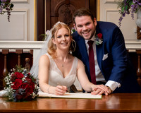 A couple smile at the camera whilst signing the wedding register within Windsor Guildhall