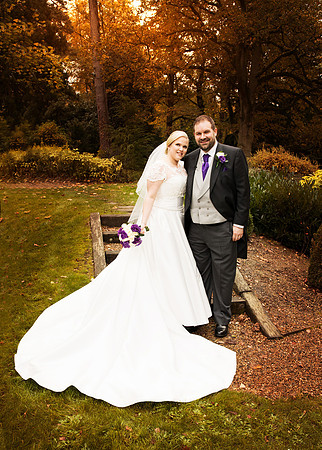 A bride & groom smile at the camera in Autumn light in the Berystede's gardens