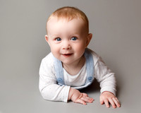 Studio photo of a baby laying on his front holding himself up and smiling