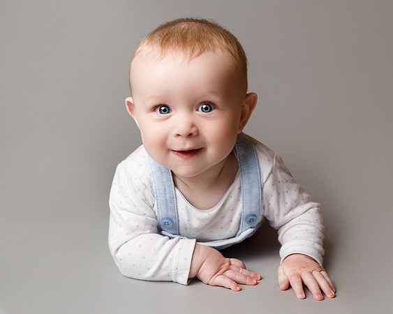 Studio photo of a baby laying on his front holding himself up and smiling