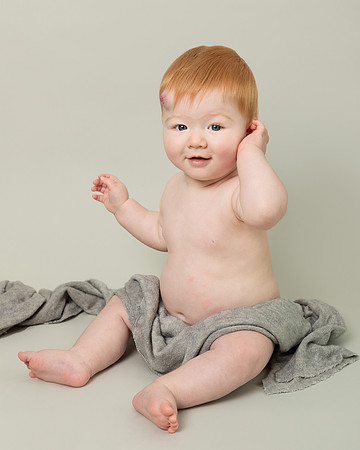 Baby boy sitting up covered only by a grey blanket