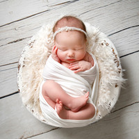 Baby wrapped up posed asleep in a bowl with fluff around her