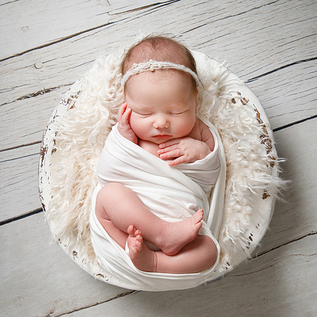 Baby wrapped up posed asleep in a bowl with fluff around her