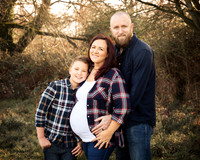 Family of three pose in an outdoor winter woodland, mum is expecting with a big baby bump