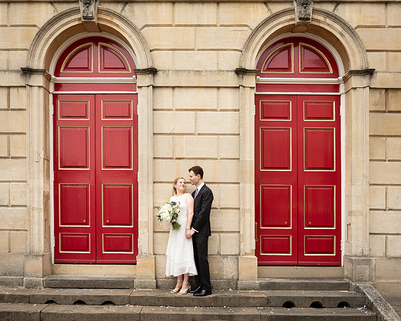 A wedding couple smile at each other in front of Windsor Guildhall's red doors